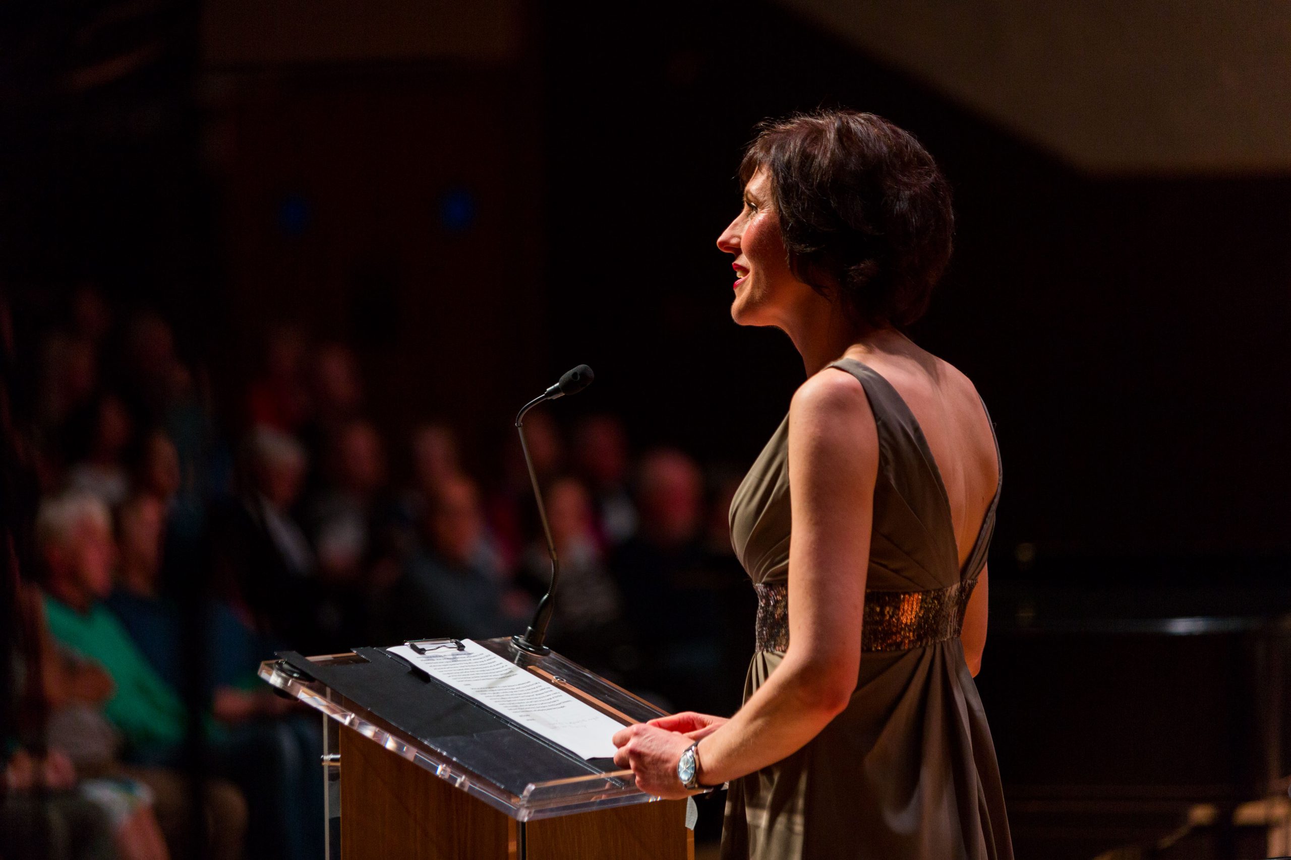 Formally dressed woman at podium under stage lights